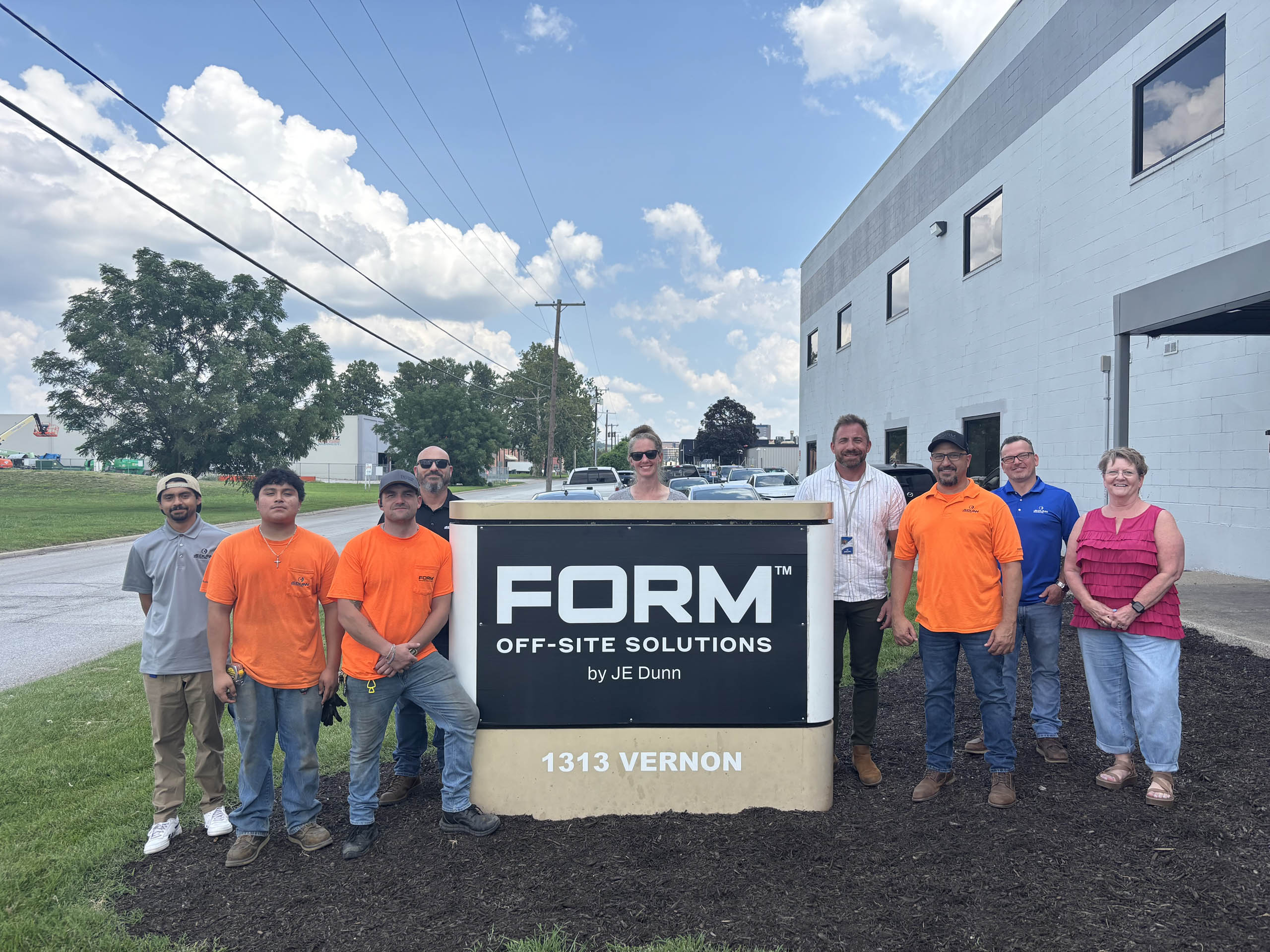 Group of ten people posing outdoors beside a FORM Off-Site Solutions sign in front of a light-gray industrial building on a sunny day.